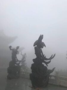 Misty stone terrace with Bodhisattva statues emerging from the fog, guiding pilgrims through hidden spiritual realms.